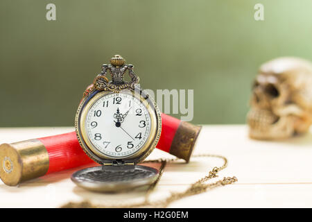 Stilleben Antike Uhr auf einen Holzboden und eine rote Shotgun Shell mit menschlichen Schädel auf dem Hintergrund platziert. Stockfoto