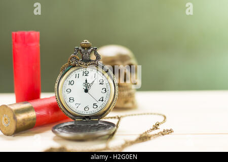 Stilleben Antike Uhr auf einen Holzboden und eine rote Shotgun Shell mit menschlichen Schädel auf dem Hintergrund platziert. Stockfoto