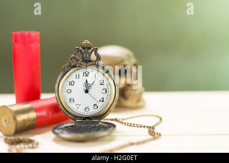 Stilleben Antike Uhr auf einen Holzboden und eine rote Shotgun Shell mit menschlichen Schädel auf dem Hintergrund platziert. Stockfoto