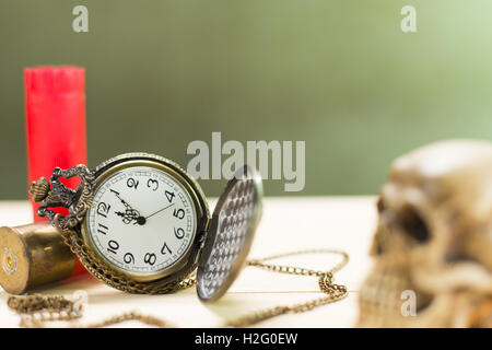 Stilleben Antike Uhr auf einen Holzboden und eine rote Shotgun Shell mit menschlichen Schädel auf dem Hintergrund platziert. Stockfoto