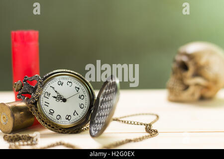Stilleben Antike Uhr auf einen Holzboden und eine rote Shotgun Shell mit menschlichen Schädel auf dem Hintergrund platziert. Stockfoto