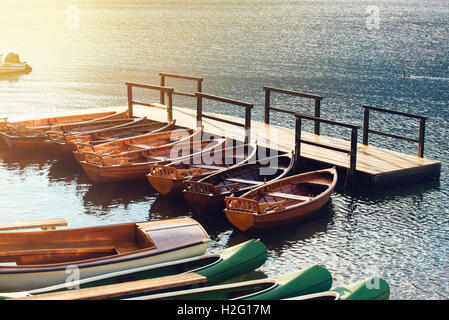 Kleine hölzerne Boote und Kanus angedockt und gebunden an leeren Pier auf dem See Stockfoto