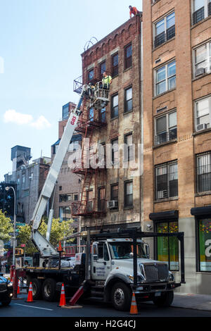 Männer, die aus einer Hubarbeitsbühne arbeiten, das Dach von einem alten Mietshaus in Soho in New York City reparieren Stockfoto