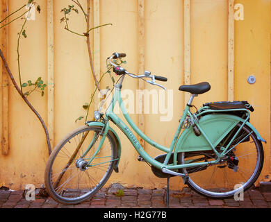 Eine einzigartige grüne Rad anliegt eine leuchtend gelbe Wand illustrieren Kopenhagen Dänemark romantische Fahrradkultur. Stockfoto