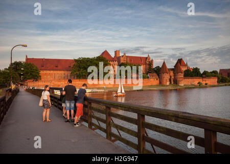 Marienburg bei Sonnenuntergang in Polen, Europa, gebaut von der deutschen Ritter-Ordens, Touristen auf der Fußgängerbrücke über den Fluss Nogat Stockfoto