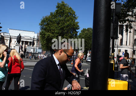 Ein Mann sieht auf seine Uhr beim Überqueren einer Straße am Trafalgar Square in London, England. Stockfoto