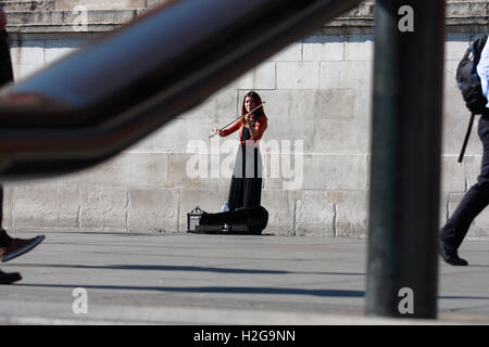 Eine Straße Entertainer spielt ihre Geige am Trafalgar Square, London, England, während die Menschen gehen übergeben. Stockfoto