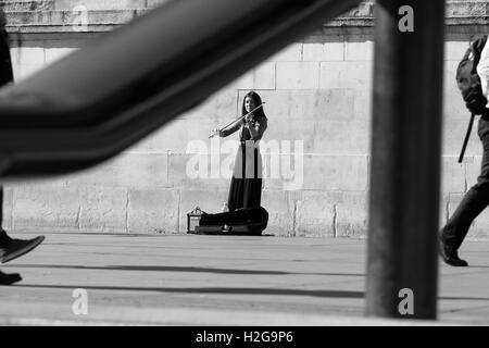 Eine Straße Entertainer spielt ihre Geige am Trafalgar Square, London, England, während die Menschen gehen übergeben. Stockfoto
