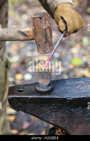 Schmied Koteletts Eisenstange mit Hammer und Meißel auf Amboss in Outdoor-ländliche Schmiede Stockfoto