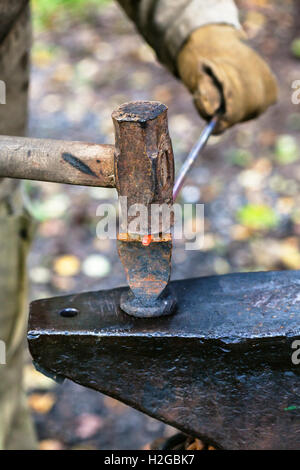 Schmied Koteletts Hot Rod mit Hammer und Meißel auf Amboss in Outdoor-ländliche Schmiede Stockfoto