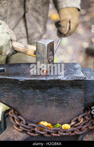 Schmied schmiedet heiße Eisenstange mit Vorschlaghammer auf Amboss in Outdoor-ländliche Schmiede Stockfoto