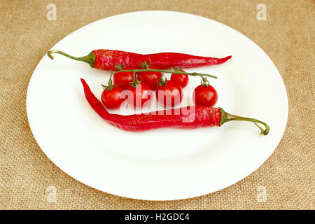 Zweig der rote Kirschtomaten und zwei Pods von Chilischoten auf dem Teller Stockfoto