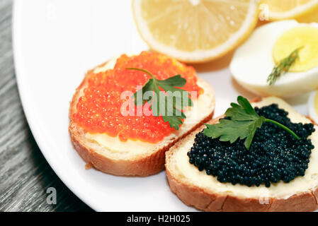 Zwei Sandwiches mit roten und schwarzen Kaviar auf Platte in der Nähe von Zitrone und Ei Stockfoto