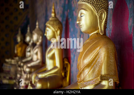 Reihe von Golden sitzenden Buddhas tragen gelbe Schärpe vor dekorative Wand in einem buddhistischen Tempel in Bangkok Thailand Stockfoto