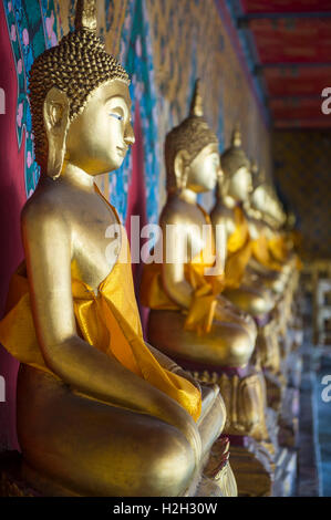 Reihe von Golden sitzenden Buddhas tragen gelbe Schärpe vor dekorative Wand in einem buddhistischen Tempel in Bangkok Thailand Stockfoto