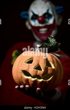 ein unheimlich böse Clown einen geschnitzten Kürbis in seiner Hand hält Stockfoto