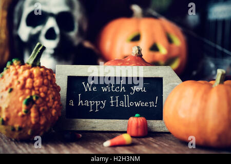 eine Tafel mit dem Text wir Hexe Sie ein happy Halloween, umgeben von einigen verschiedenen Kürbissen, platziert auf einem rustikalen hölzernen Surf Stockfoto