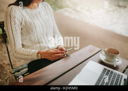 Schuss von junge Frau sitzt im Café im Freien mit Handy zugeschnitten. Sitzen im Café-Tisch mit Laptop und Handy ich weiblich Stockfoto