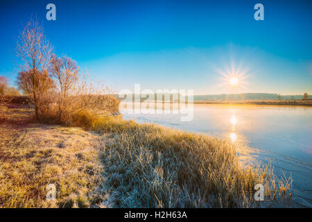 Sun Rises über River. Herbst Frost gefrorenen Fluss mit Thin Ice Grass bedeckt bedeckt mit Frost. Sonnenaufgang, Sonnenuntergang über Herbst Riv Stockfoto