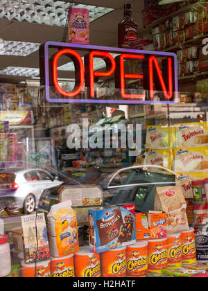 Schaufenster der Convenience-Store mit Schild "geöffnet" in Neonlicht. Verschiedene Produkte und Süßigkeiten im Angebot unten.