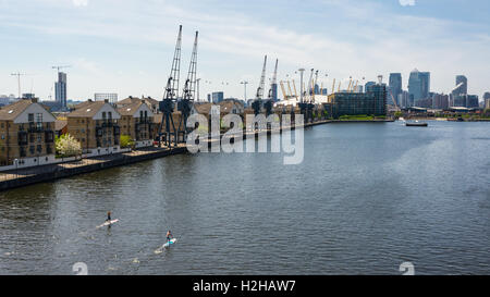 Der London Royal Docks im Osten von London gelegen, mit zwei Personen Paddeln in es und Häuser am Wasser gebaut. Stockfoto