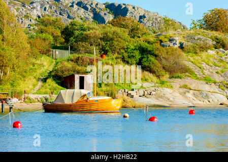 Alten Holzmotorboot mit Segeln Mast vor Anker im Meer, die Bucht in der Nähe von Felsen und Gebüsch. Stockfoto