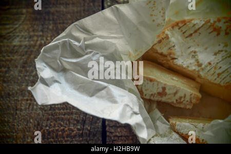 Camembert auf zerknüllte Geschenkpapier auf hölzernen Hintergrund. Grunge-Stil. Stockfoto