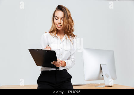 Attraktive junge lächelnde Geschäftsfrau Signieren von Dokumenten im Büro Stockfoto