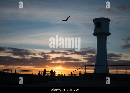 Fischer und ein Leuchtturm sind gegen einen wunderschönen Sonnenuntergang am Hafen von Littlehampton, West Sussex, England Silhouette. Stockfoto