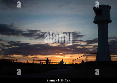 Fischer und ein Leuchtturm sind gegen einen wunderschönen Sonnenuntergang am Hafen von Littlehampton, West Sussex, England Silhouette. Stockfoto