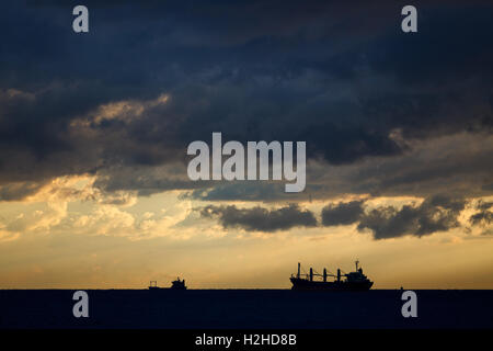 Frachtschiffe am Meer in den Strahlen der untergehenden Sonne und dramatische Wolken Stockfoto