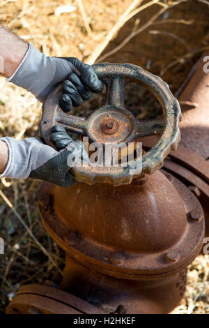 Hände mit Arbeitshandschuhen umklammert ein Rohr Ventil von einem sehr alten und Rusty Water line Stockfoto