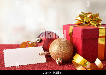 Xmas Dekoration mit Tag, rote Geschenkbox und goldenes Band und zwei Kugeln auf hellrot strukturierten Tabelle und weißen Hintergrund. Vorne Stockfoto