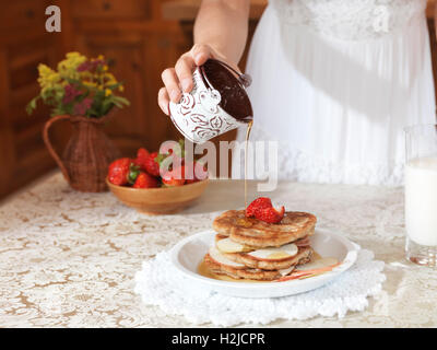 Nahaufnahme einer Frau die hand strömenden Ahornsirup auf Pfannkuchen mit Erdbeeren und Äpfel Stockfoto