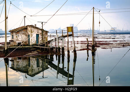 Alte Fischerei Haus reflektiert in der Lagune von Marina di Ravenna, industrielle Hafen im Hintergrund. Stockfoto