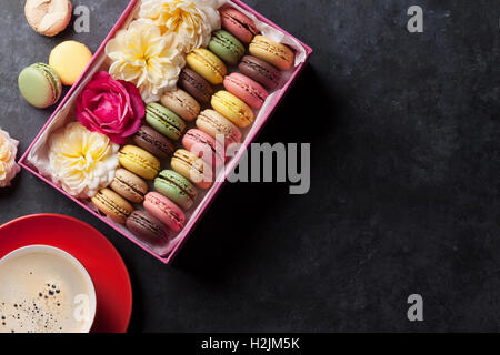 Bunte Makronen und Kaffee am Steintisch. Süßen Macarons in Geschenk-Box und Blumen. Draufsicht mit Textfreiraum Stockfoto