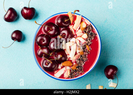 Smoothie-Schüssel mit frischen schwarzen Kirschen, Kokosflocken, Mandeln und Kakao Nibs. Ansicht von oben. Textfreiraum Stockfoto