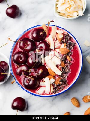 Smoothie-Schüssel mit frischen schwarzen Kirschen, Kokosflocken, Mandeln. Marmor-Hintergrund. Ansicht von oben. Stockfoto