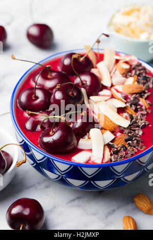 Smoothie-Schüssel mit frischen schwarzen Kirschen, Kokosflocken, Mandeln und Kakao Nibs. Marmor-Hintergrund Stockfoto