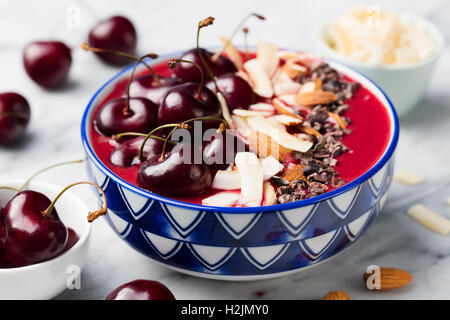 Smoothie-Schüssel mit frischen schwarzen Kirschen, Kokosflocken, Mandeln und Kakao Nibs. Marmor-Hintergrund Stockfoto
