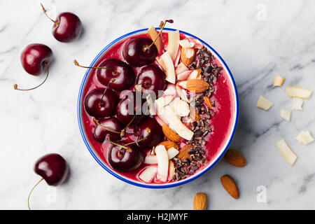 Smoothie-Schüssel mit frischen schwarzen Kirschen, Kokosflocken, Mandeln. Marmor-Hintergrund. Ansicht von oben. Stockfoto