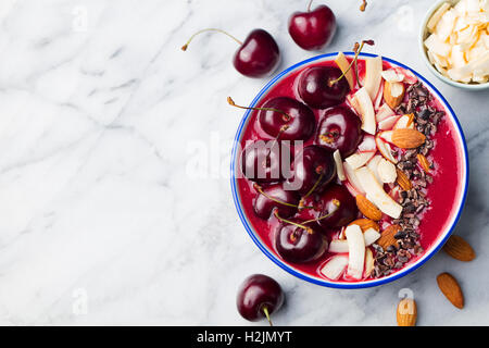 Smoothie-Schüssel mit frischen schwarzen Kirschen, Kokosflocken, Mandeln und Kakao Nibs. Ansicht von oben. Textfreiraum Stockfoto