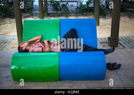 Ein junger malaysischer Mann nimmt ein Nickerchen auf einer Parkbank in Kuala Lumpur, Malaysia, Südost-Asien. Stockfoto