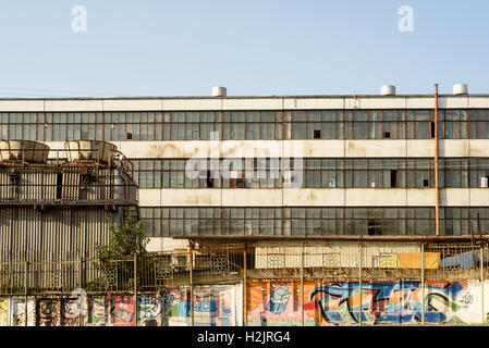 Moderne städtische Graffiti gegen ein ehemaliges Fabrikgebäude mit blauem Himmelshintergrund Stockfoto