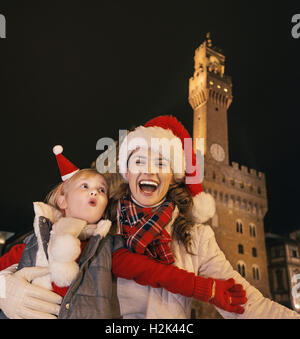 Reise voller Inspiration in der Weihnachtszeit in Florenz. Porträt der lächelnde junge Mutter und Tochter Touristen in Weihnachtsmützen gegen Palazzo Vecchio in Florenz, Italien Spaß Zeit Stockfoto