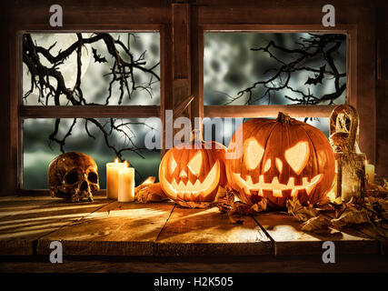 Gruselige Halloween-Kürbisse auf Holzplanken, vor Fenster mit beängstigend Hintergrund platziert Stockfoto