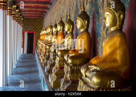 Reihe von Golden sitzenden Buddhas tragen gelbe Schärpe vor dekorative Wand in einem buddhistischen Tempel in Bangkok Thailand Stockfoto