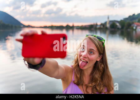 Junge Frau, die die Selfie mit ausgestreckten Zunge, Schliersee, Upper Bavaria, Bavaria, Germany Stockfoto