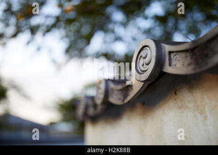 Eine Detail-Aufnahme der Kante von einem japanischen keramische Dachziegel auf einer alten Mauer mit einem weichen, unscharfen Hintergrund Himmel und Bäume. Stockfoto