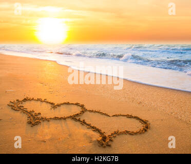 zwei hand gezeichnete Herzen am Strandsand über Sonnenuntergang Stockfoto